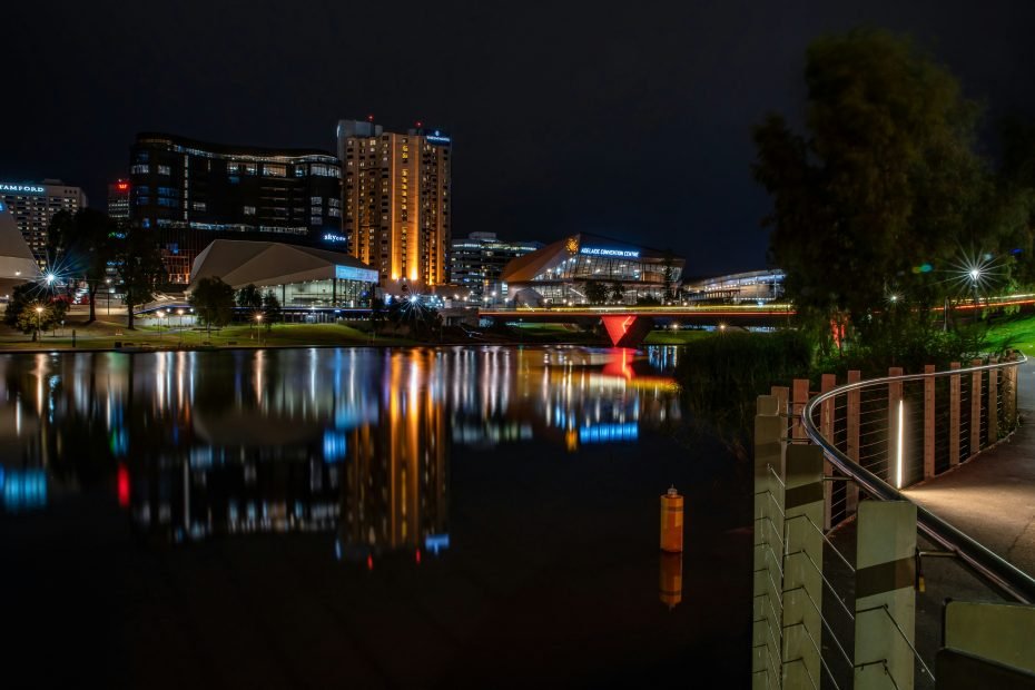 阿德莱德城市夜景，灯火辉煌的建筑倒映在静谧的河面上，展现出南澳大利亚州首府城市的繁华与宁静。